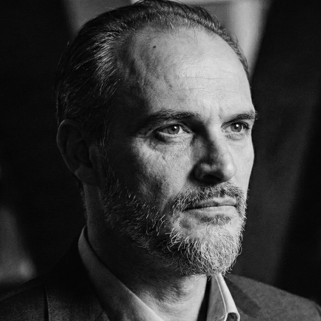 Der Mann mit grauem Bart und ernstem Blick, professionell in Schwarz-Weiß fotografiert.