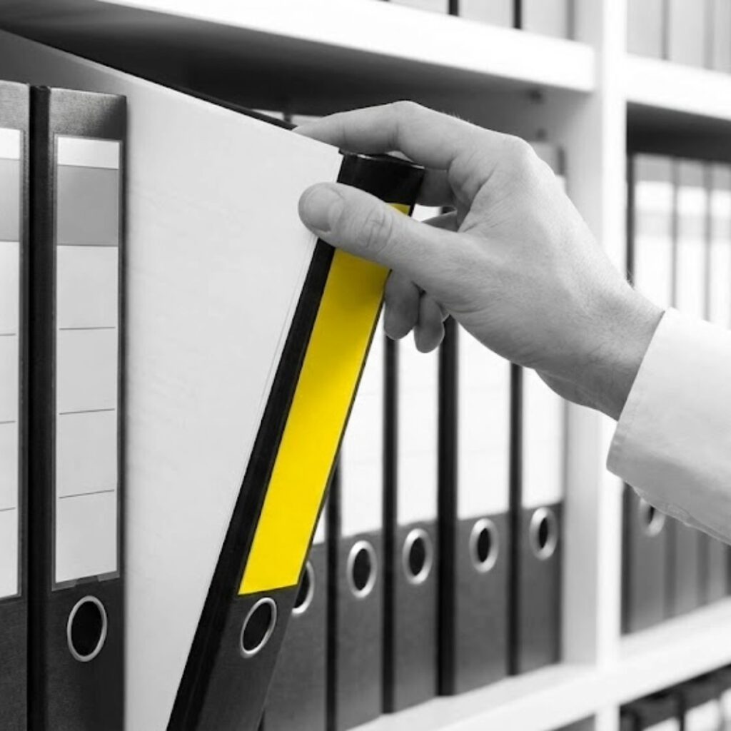 Hand zieht gelben Aktenordner aus einem Regal, Büroorganisation, Archiv, Dokumentenmanagement.